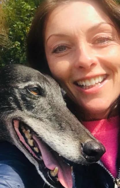 Lorraine smiling outdoors with her own rescued greyhound