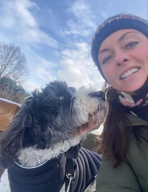 Lorraine smiling on a winter dog walk with a shaggy black and white dog